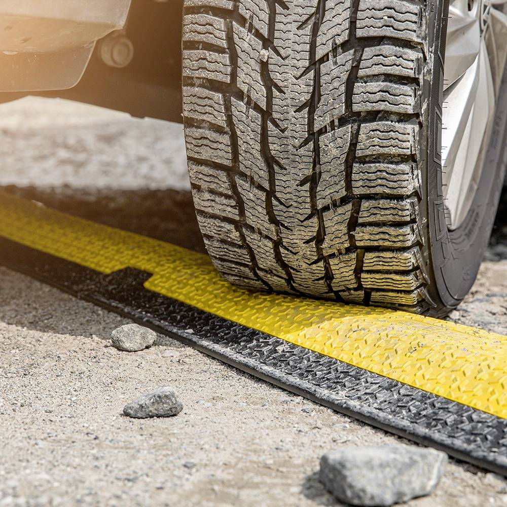 Opona samochodu przekracza żółtą krawędź na asfaltowej drodze, otoczona małymi kamieniami. Obrazuje to bezpieczeństwo ruchu drogowego.