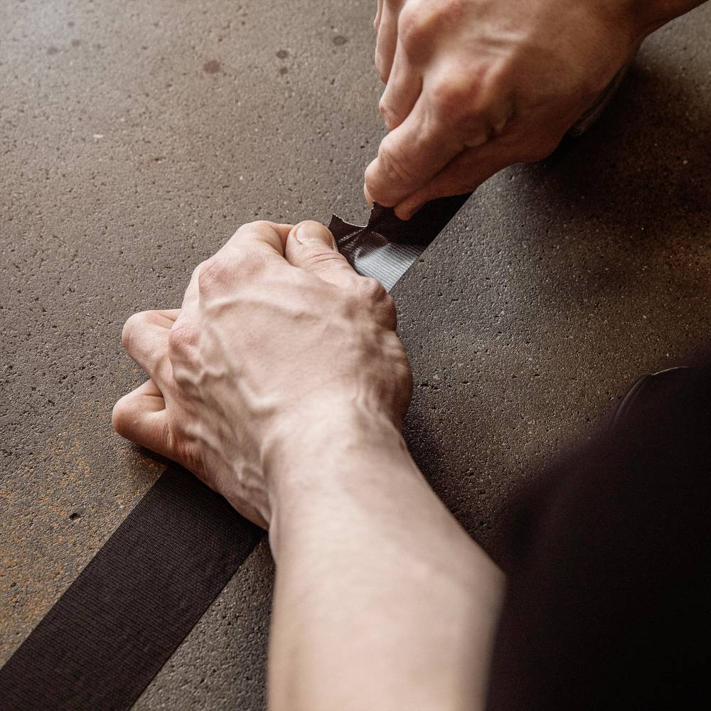 Osoba mocuje czarną taśmę klejącą na powierzchni. Jej ręce są widoczne i skupione, starannie przyklejając taśmę.