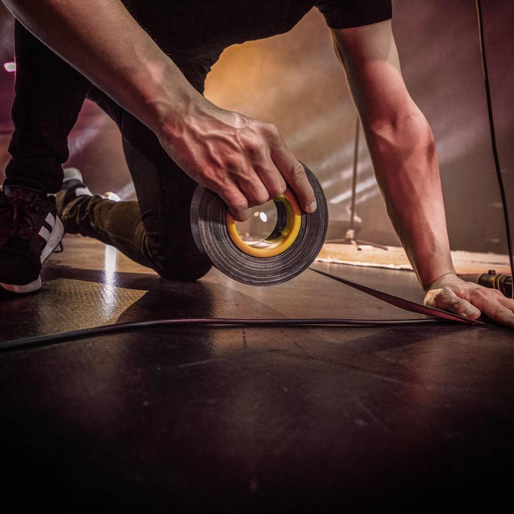 Osoba trzyma rolkę taśmy klejącej na scenie, przygotowana do przeprowadzenia napraw podczas wydarzenia.