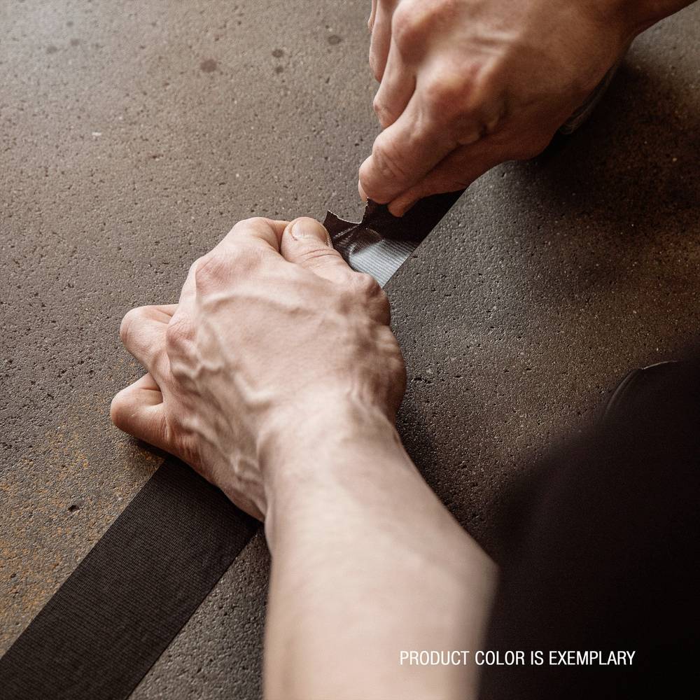 Dwie ręce napinają czarną taśmę klejącą na brązowej powierzchni. Tekst w rogu głosi: 'Kolor produktu jest wzorcowy'.