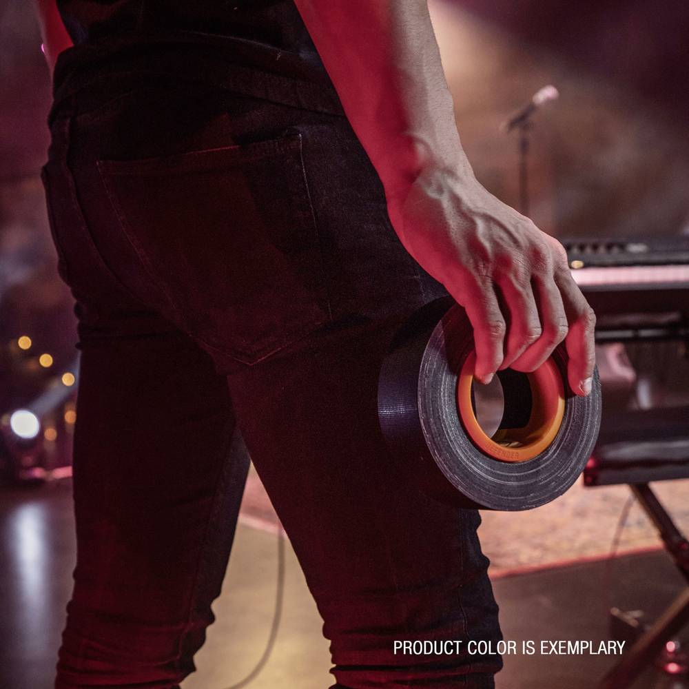 Osoba na scenie trzyma rolkę taśmy klejącej. W tle, niewyraźnie widoczne są keyboard i mikrofon.