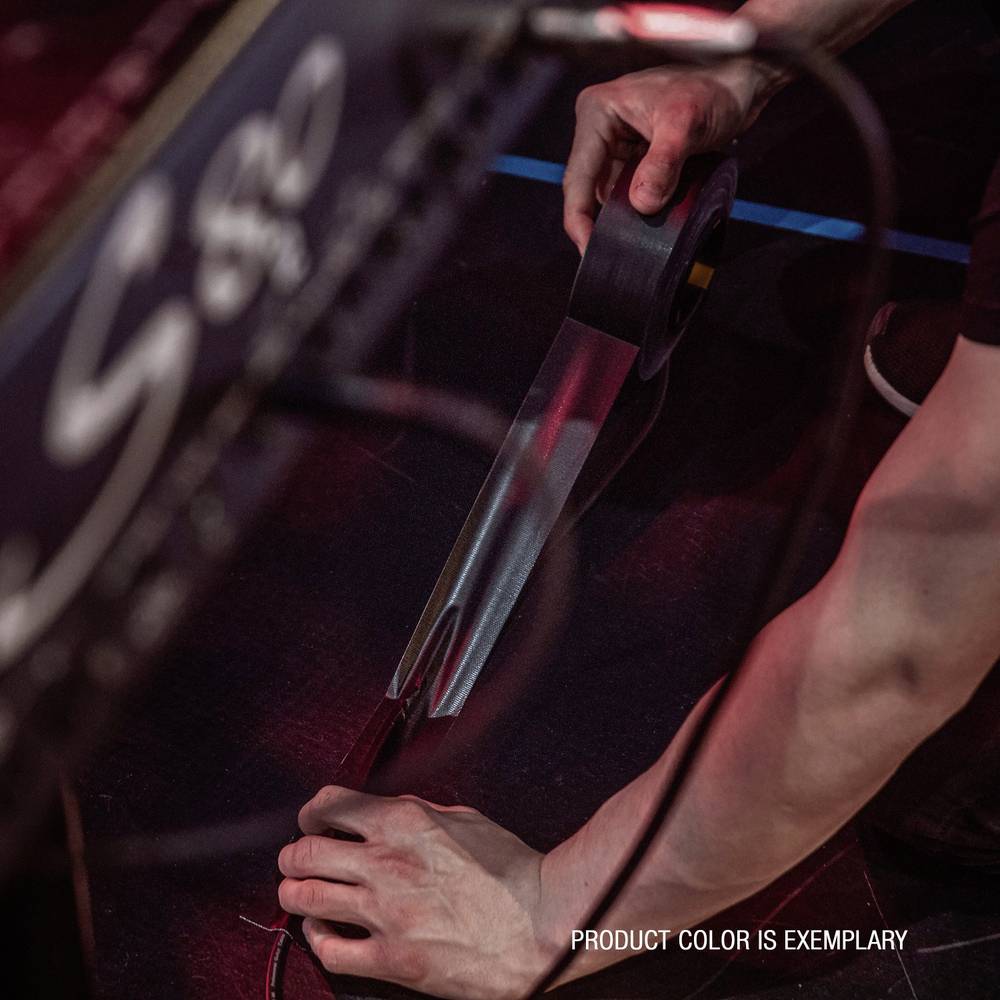 Osoba używa dyspensera do taśmy klejącej, aby coś przymocować lub zabezpieczyć. Tekst na obrazku: 'KOLOR PRODUKTU JEST PRZYKŁADOWY'.