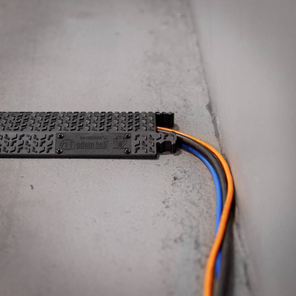 Naziemne zabezpieczenie przewodów chroni pomarańczowe i niebieskie kable wzdłuż ściany.