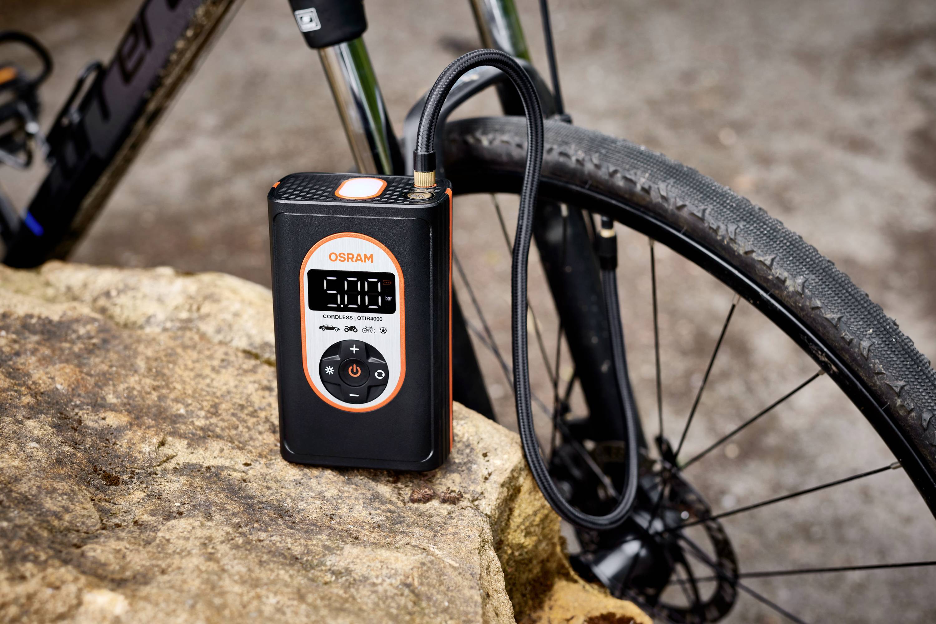 Elektryczna pompka rowerowa z cyfrowym wyświetlaczem umieszczona na kamieniu. Wyświetlacz pokazuje '5.0'.