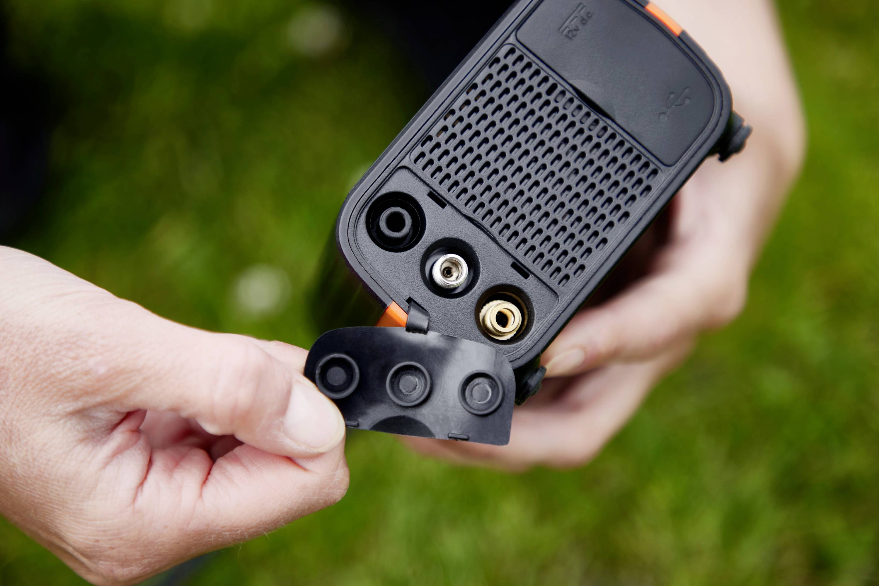 Osoba trzyma w ręku urządzenie z odkrytymi złączami. Złącza są dostępne przez klapkę ochronną. Urządzenie posiada wentylowaną konstrukcję.