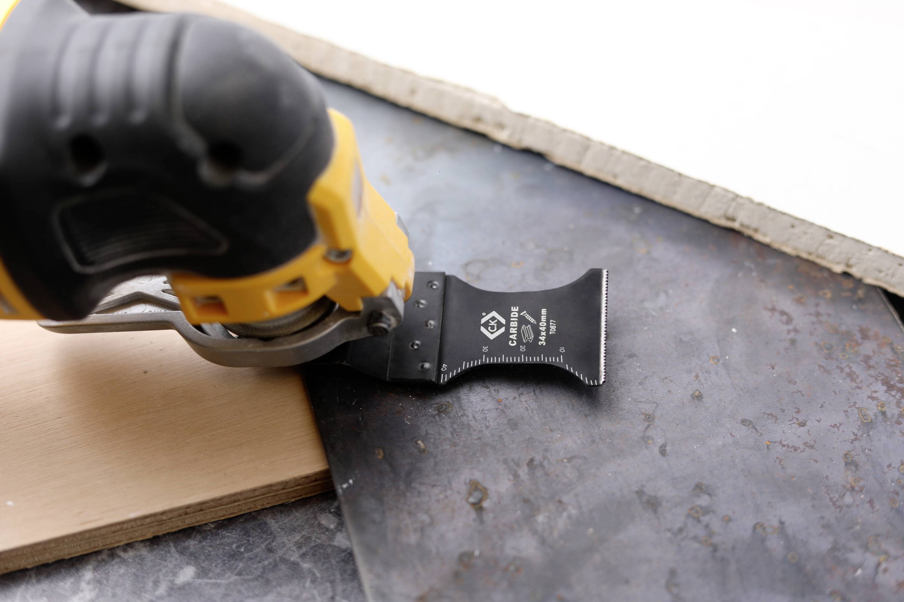 Elektronarzędzie z oscylującym ostrzem piły przecina cienką warstwę metalu obok deski drewnianej.