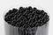 Okrągły pojemnik pełen czarnych pisaków, ułożonych równomiernie i schludnie, sfotografowany z góry na białym tle.