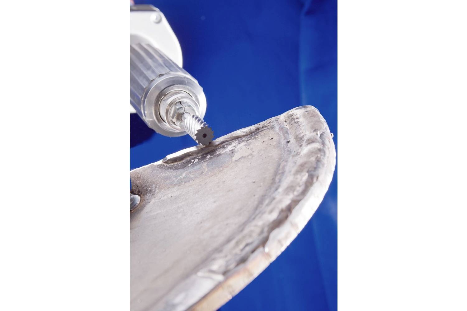 Urządzenie szlifierskie obrabia krawędź kawałka metalu na niebieskim tle.