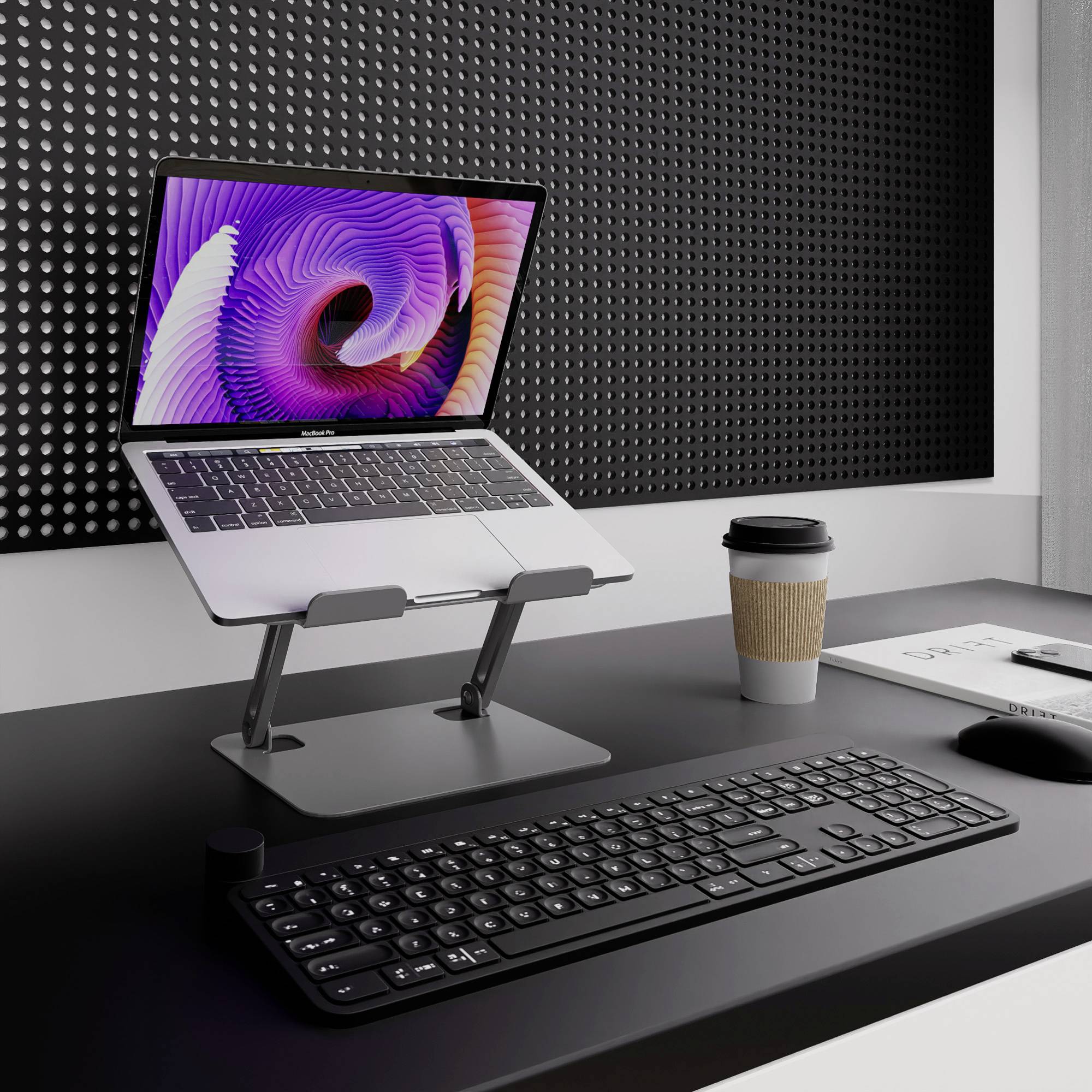 Laptop stoi na stole z podstawką, obok niego filiżanka i mysz komputerowa, w tle czarna tablica.