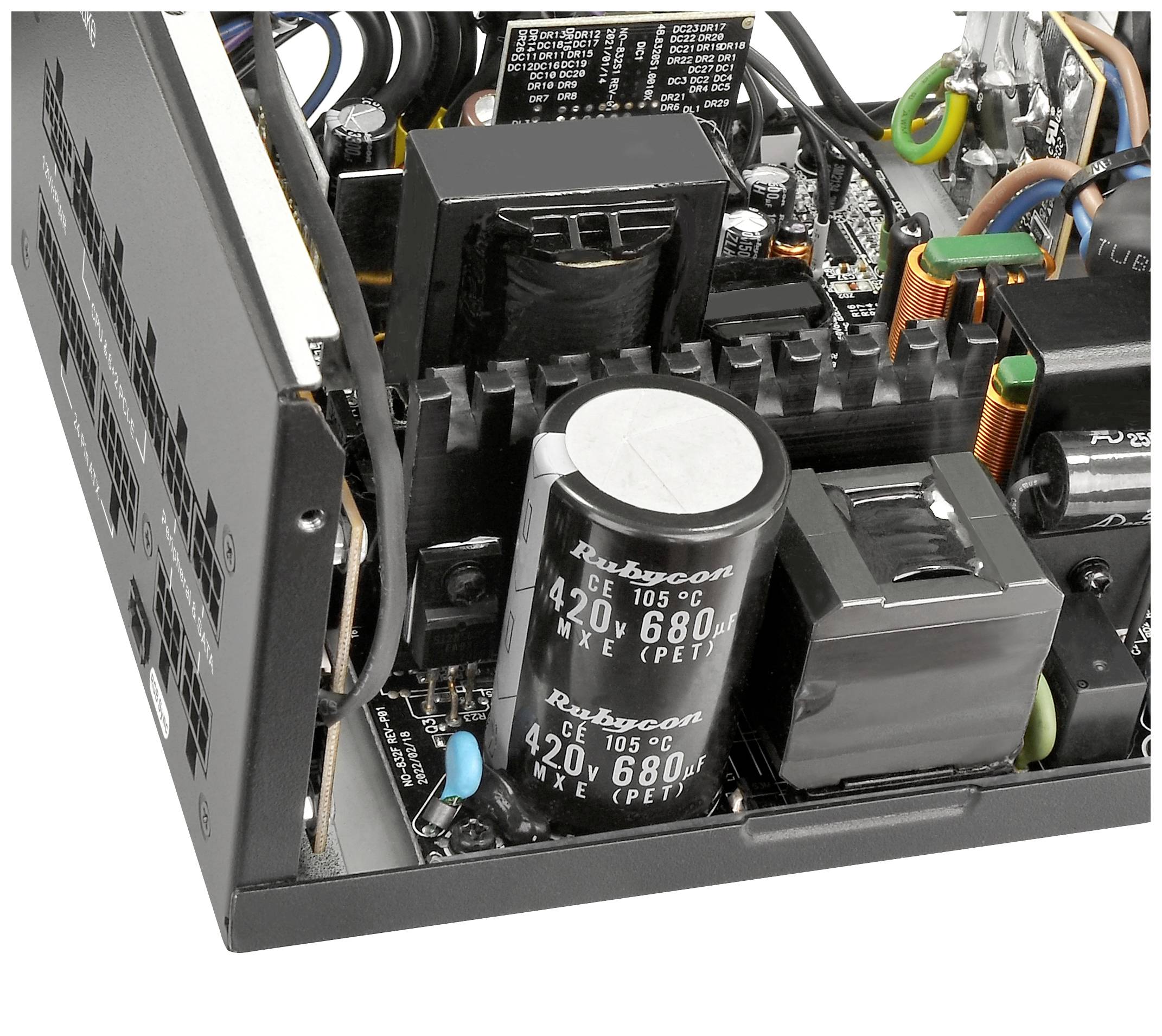 Widok wnętrza zasilacza z kondensatorami, płytą główną i kablami. Prezentuje budowę elektryczną i komponenty zasilacza komputerowego.