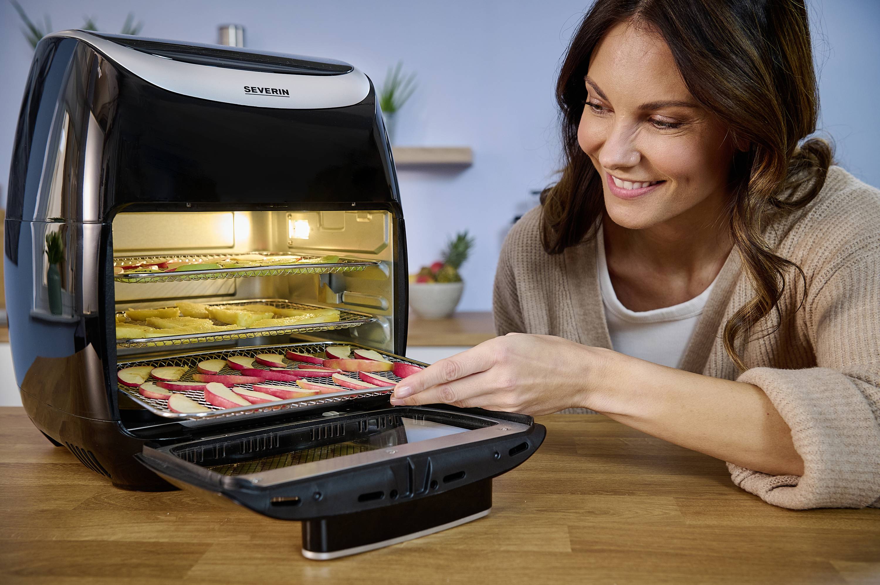 Kobieta piecze ciasteczka w piekarniku na gorące powietrze na drewnianym stole, uśmiechając się zadowolona.