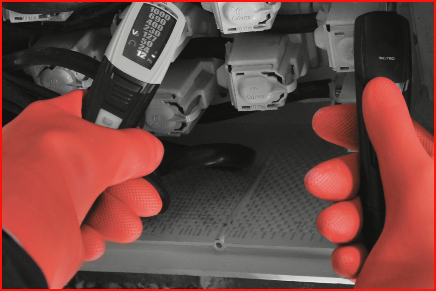 Technik w czerwonych rękawicach ochronnych trzyma przyrządy pomiarowe przed rzędem elektrycznych złączy.