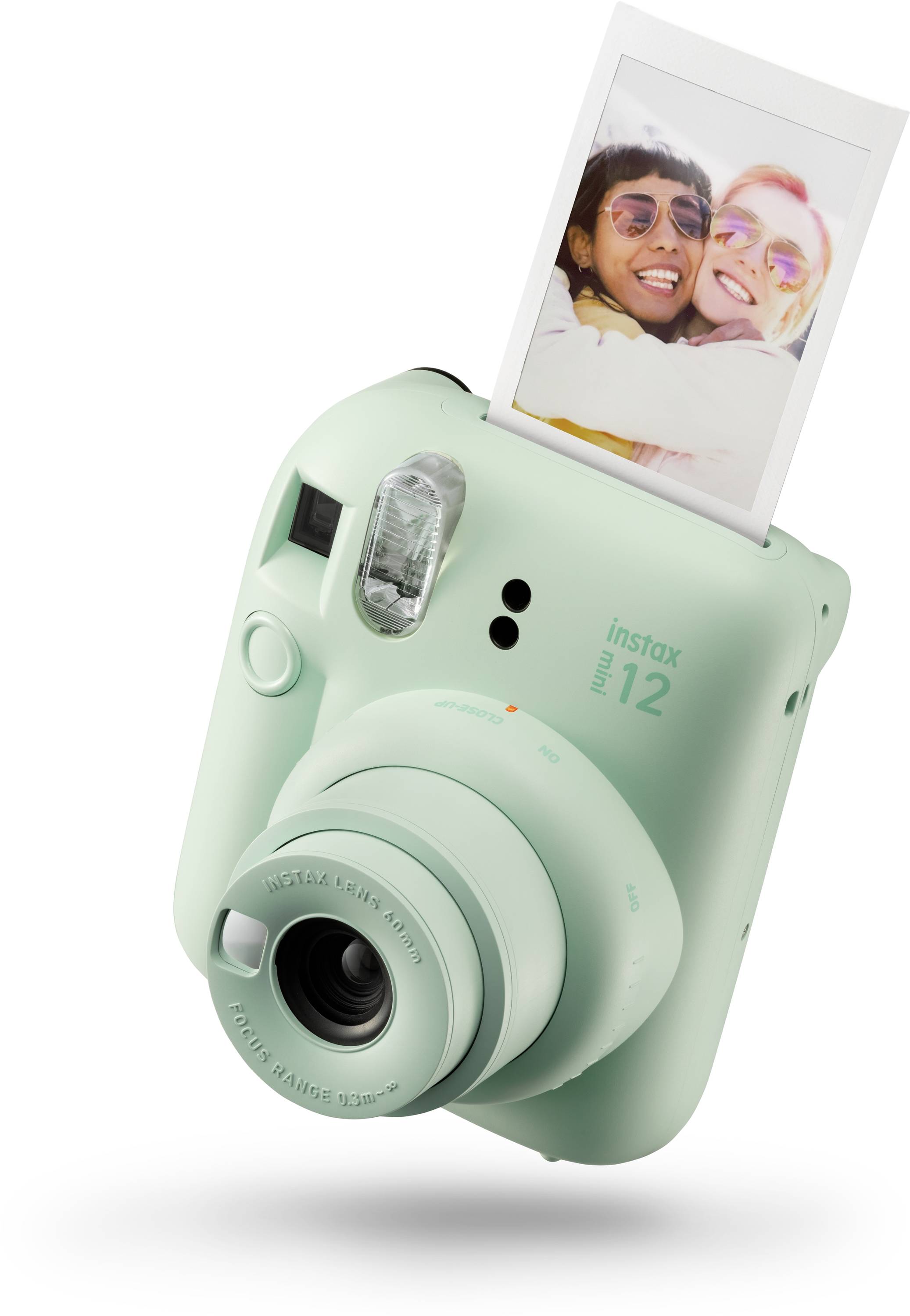 Mini aparat fotograficzny z funkcją natychmiastowego wydruku drukuje zdjęcie przedstawiające dwie uśmiechnięte osoby. Aparat jest miętowozielony i ma nadruk 'instax mini 12'.