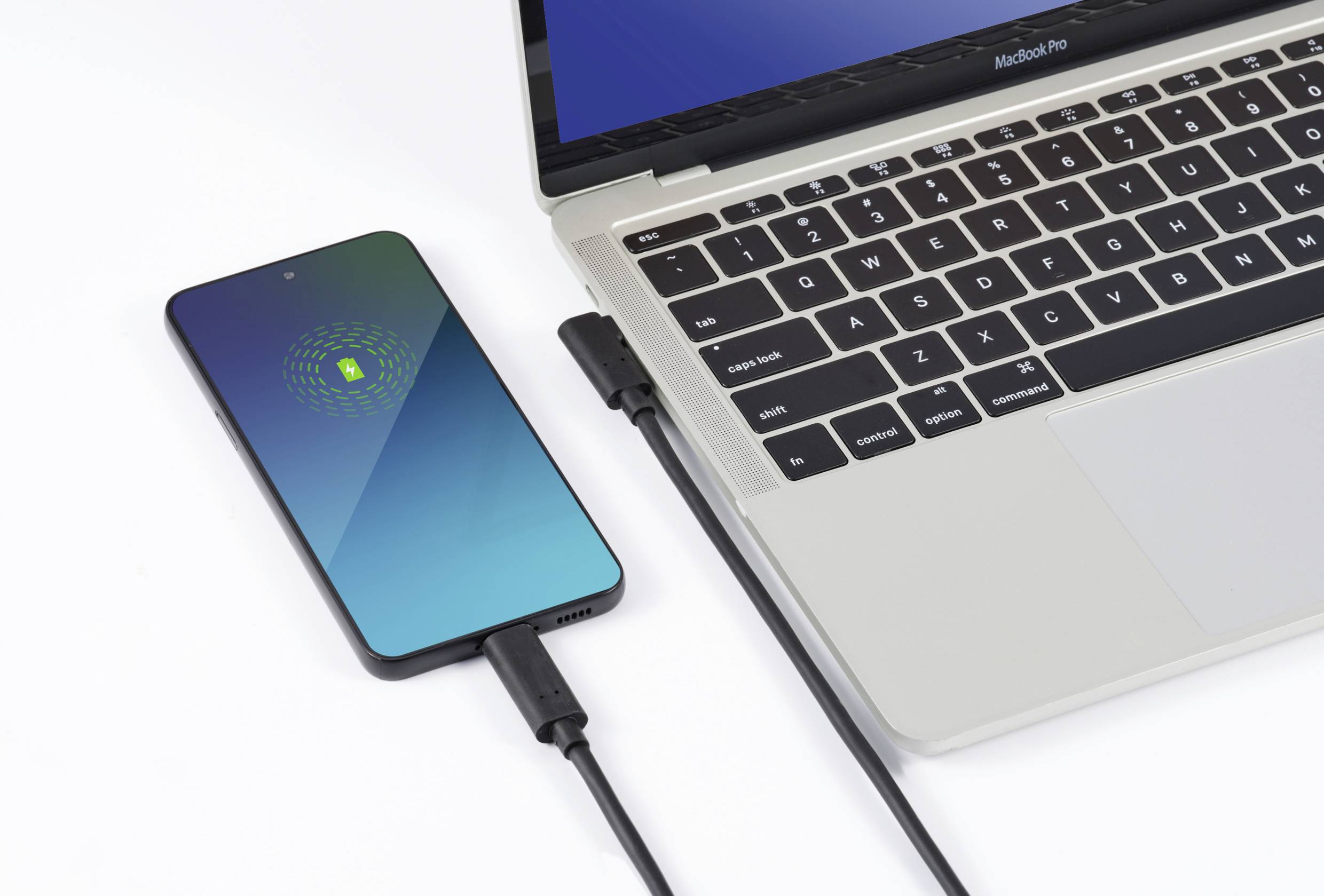 Smartfon jest podłączony do laptopa za pomocą kabla USB i ładowany. Ekran ładowania wyświetla zieloną ikonę baterii.