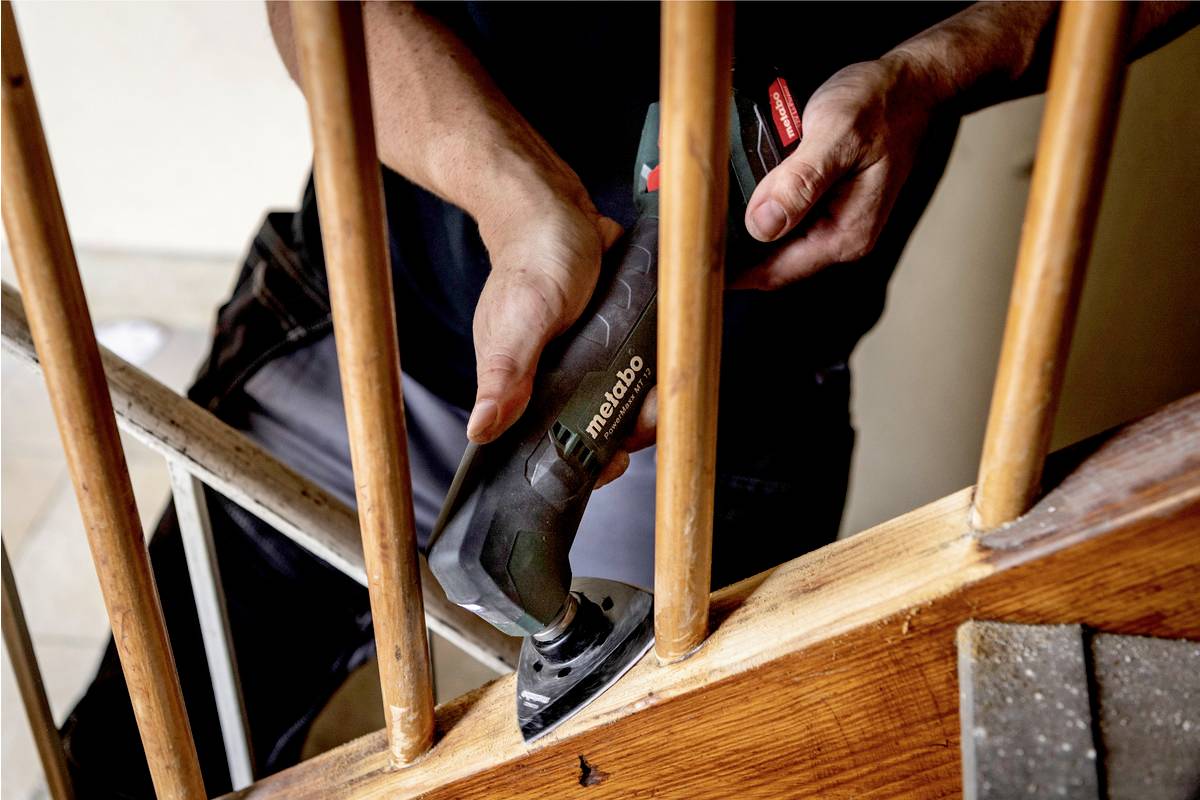 Osoba szlifuje drewnianą poręcz za pomocą narzędzia szlifierskiego Metabo, aby ją wygładzić lub odnowić.