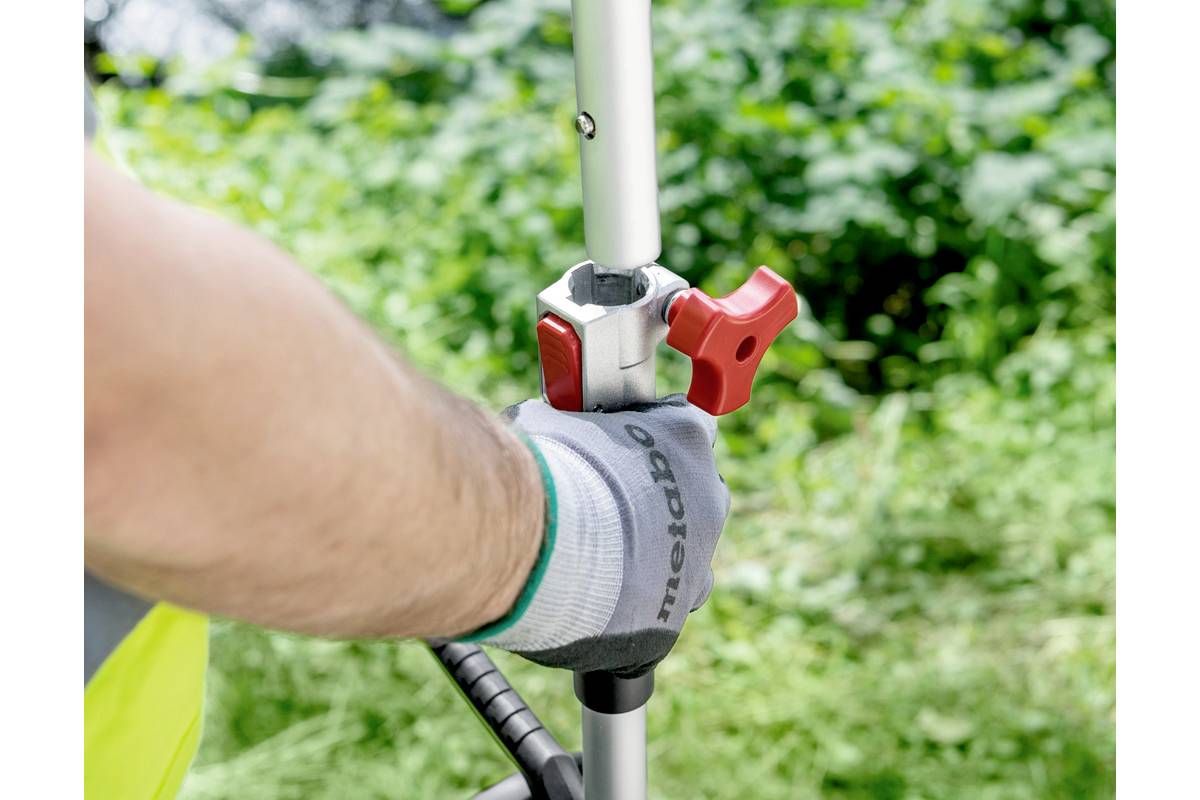 Dłoń w rękawiczce reguluje czerwony uchwyt na metalowym pręcie na zielonym tle.