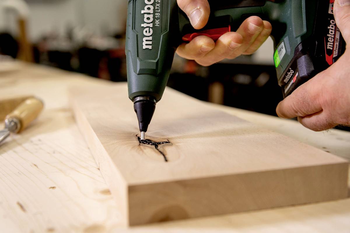 Osoba wierca dziurę w desce drewnianej za pomocą wiertarki elektrycznej.