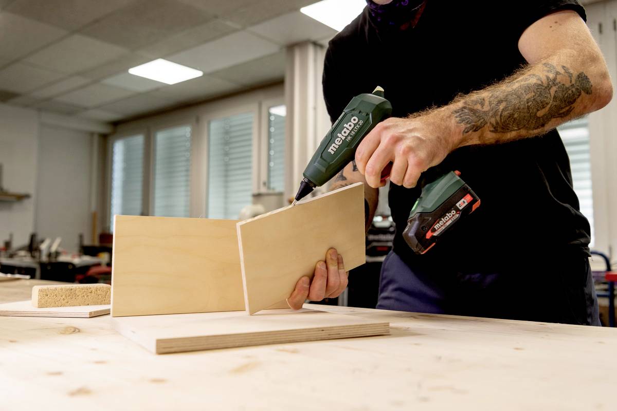 Osoba używa wkrętarki akumulatorowej do skręcania dwóch desek drewnianych w warsztacie.