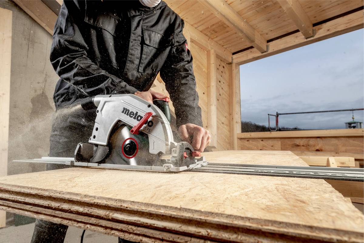 Robotnik przecina drewnianą płytę ręczną piłą tarczową w konstrukcji drewnianej. Nosi odzież ochronną.