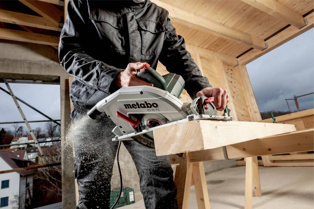 Mężczyzna przecina drewnianą deskę elektryczną ręczną piłą tarczową na placu budowy. Na zewnątrz widać pochmurną pogodę.