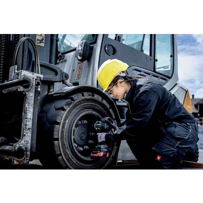 Osoba w stroju roboczym i kasku ochronnym naprawia koło ciężkiego pojazdu za pomocą elektronarzędzia.