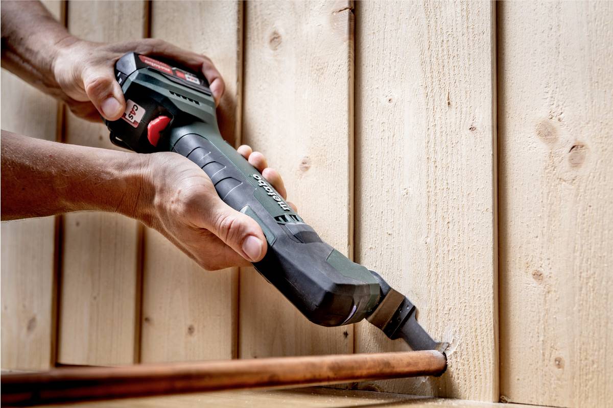 Rzemieślnik używa elektrycznego wielofunkcyjnego narzędzia do obróbki spoiny w drewnianej boazerii.
