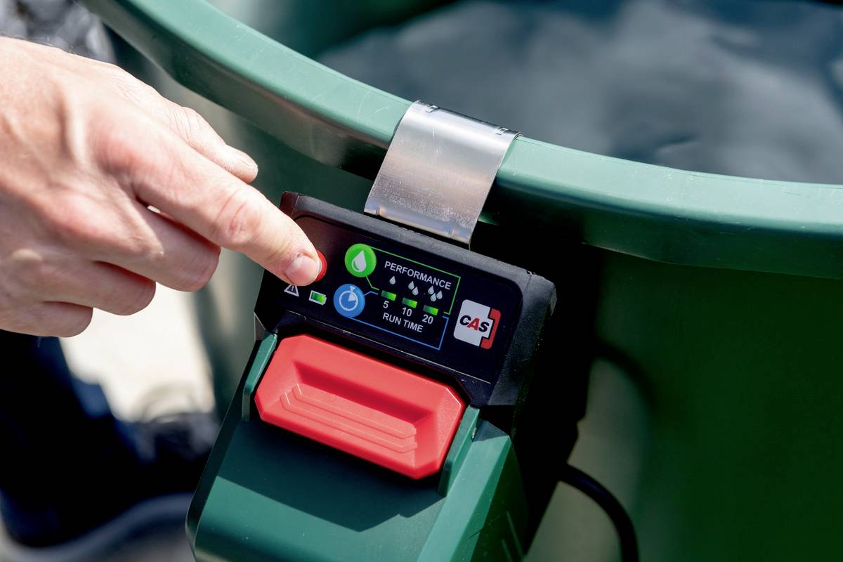 Osoba obsługuje przycisk zielonego urządzenia ogrodowego z wyświetlaczem, który pokazuje tryby pracy i czas działania, na przykład w opryskiwaczu ogrodowym.