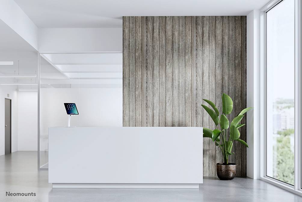 Recepcja z białym ladą, zieloną rośliną doniczkową i ścianą wyłożoną drewnianymi panelami. Po lewej stronie lady leży tablet.