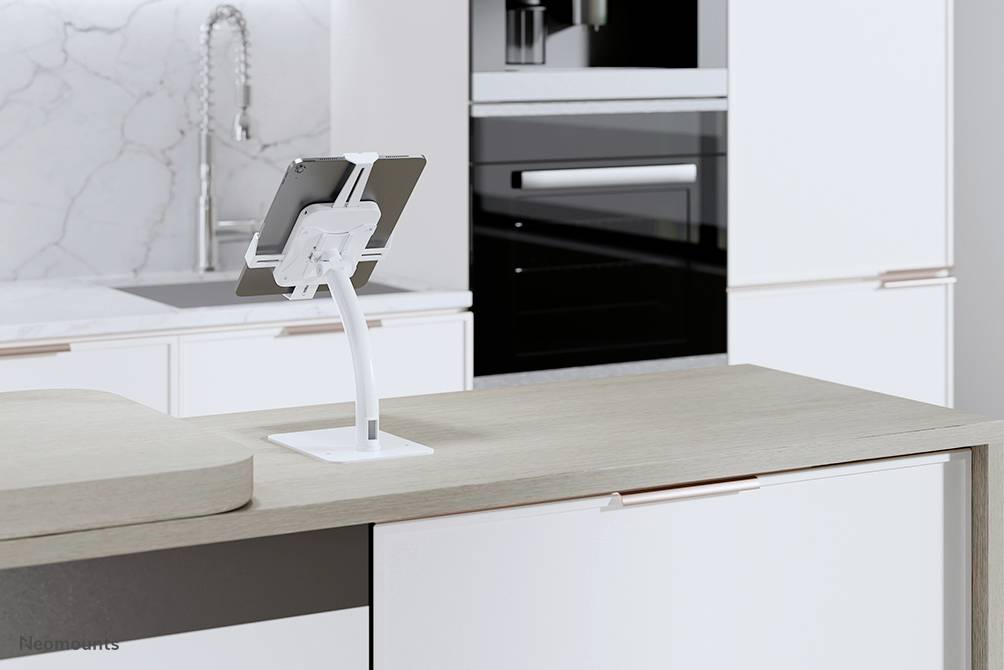 Tablet na białym stojaku na nowoczesnym blacie kuchennym. W tle widoczne białe szafki i kran.