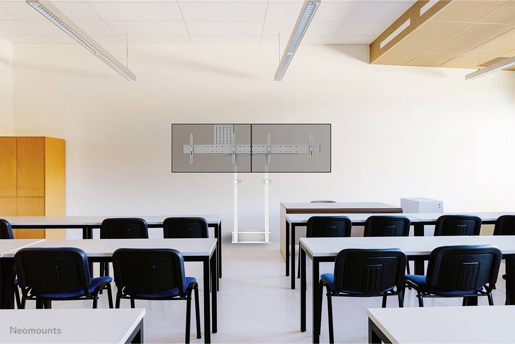 Pusty pokój lekcyjny z ławkami i krzesłami. Z przodu stoi duży monitor na podstawce. Pomieszczenie jest jasno oświetlone.