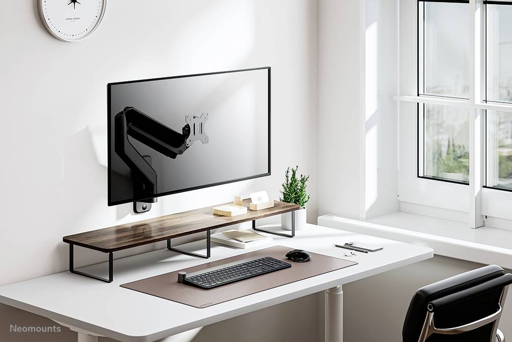 Minimalistyczne stanowisko pracy z monitorem zamontowanym na ścianie, klawiaturą i myszką na białym stole obok okna.