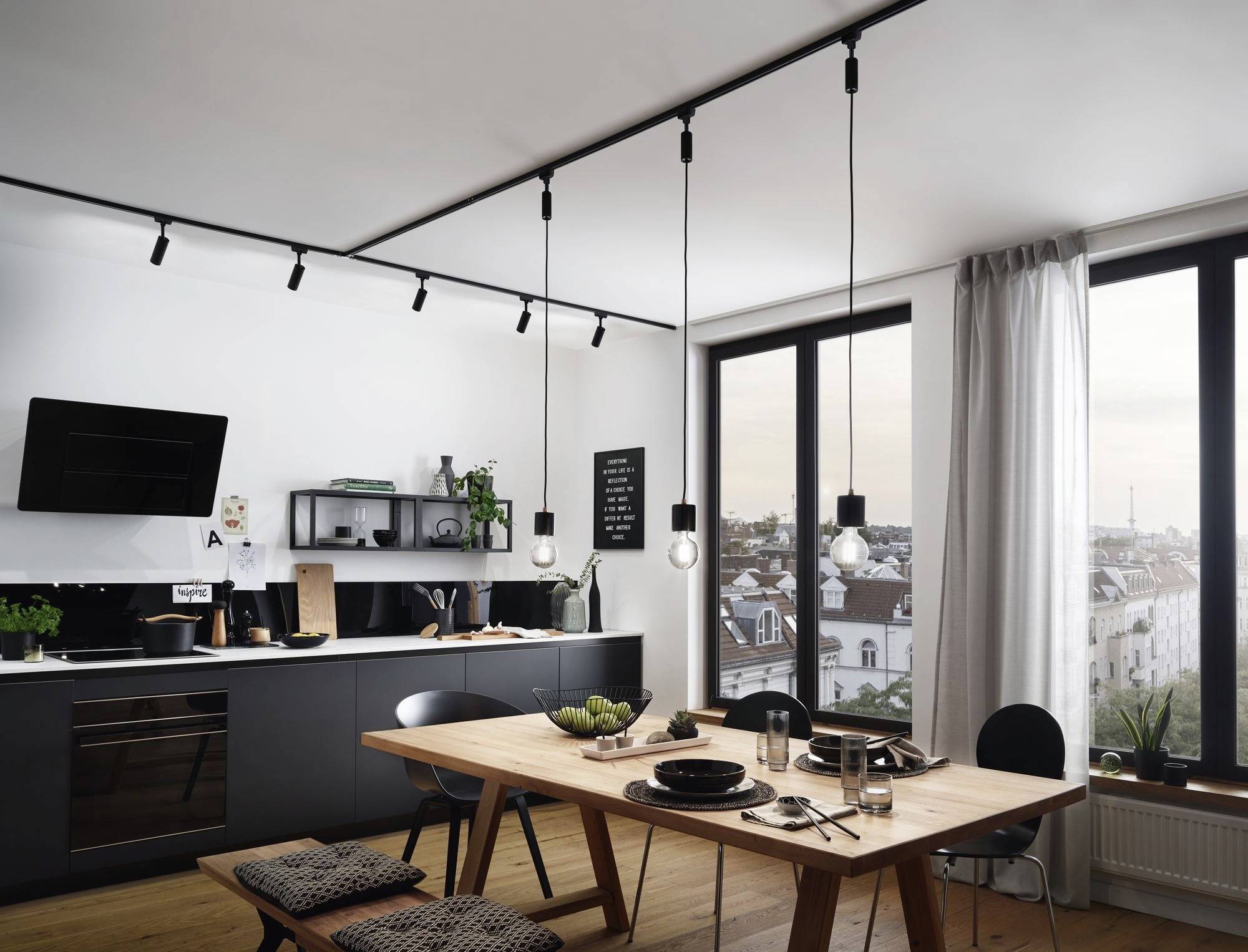 Nowoczesna kuchnia z drewnianym stołem jadalnianym, wiszącymi lampami, dużymi oknami, widokiem na miasto, ciemnymi szafkami i zielonymi roślinami.