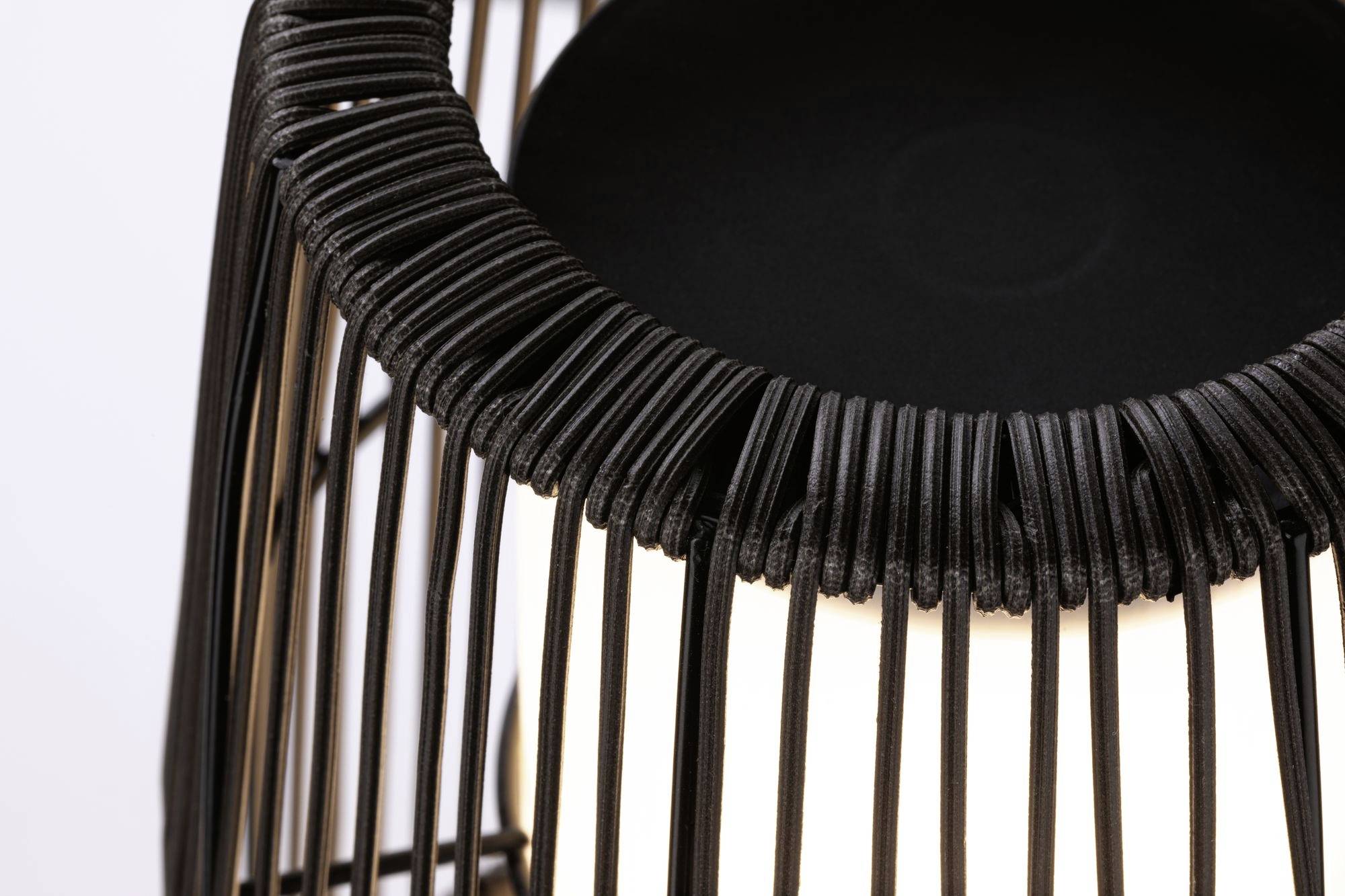 Czarna, pleciona oprawa lampy z widoczną żarówką. Nowoczesny design koncentrujący się na strukturze tekstylnej i oświetleniu.