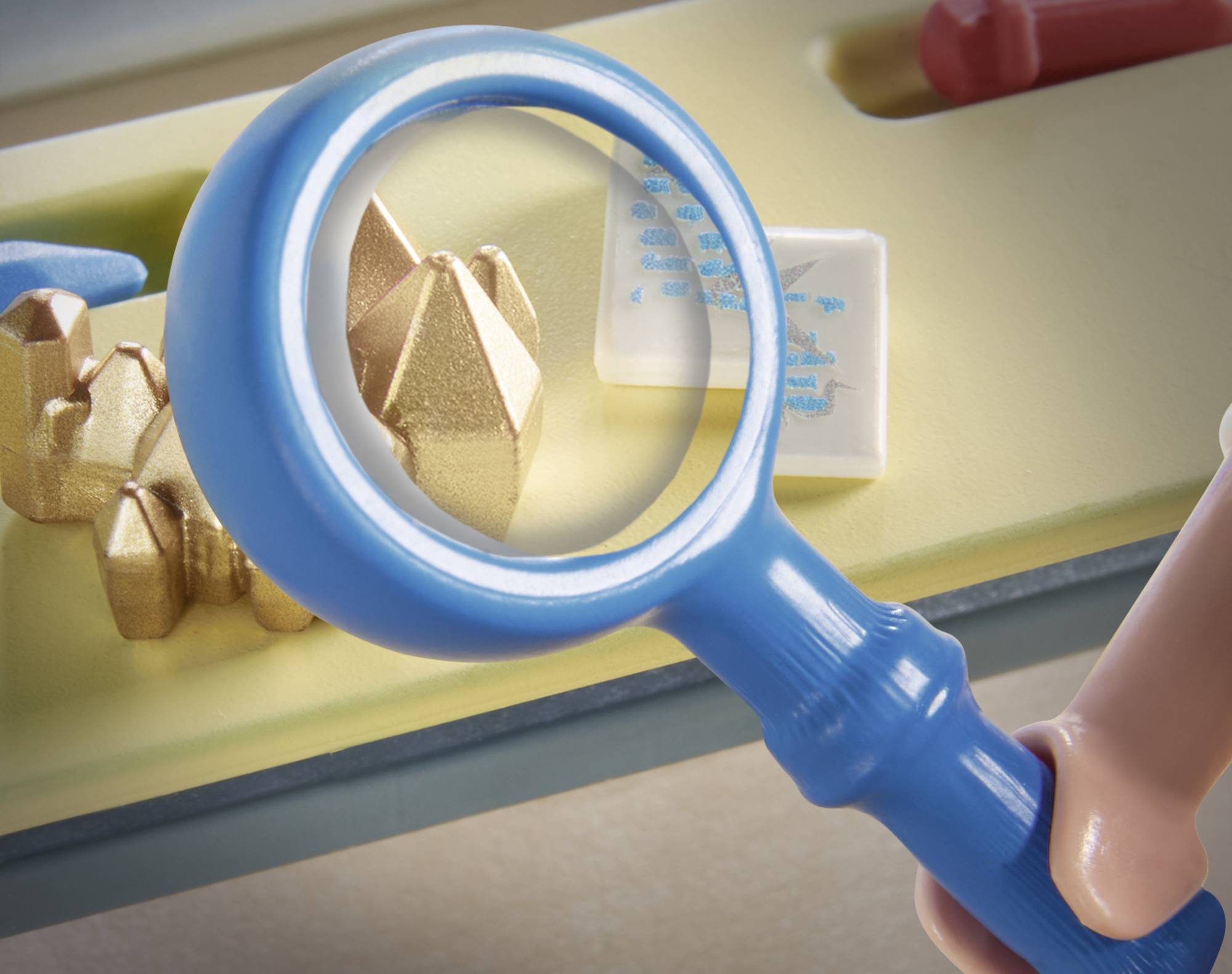 Niebieska lupa powiększa mały, złoty model na tle. Po prawej stronie widoczne są szczegóły obiektu przypominającego humanoidalną formę.