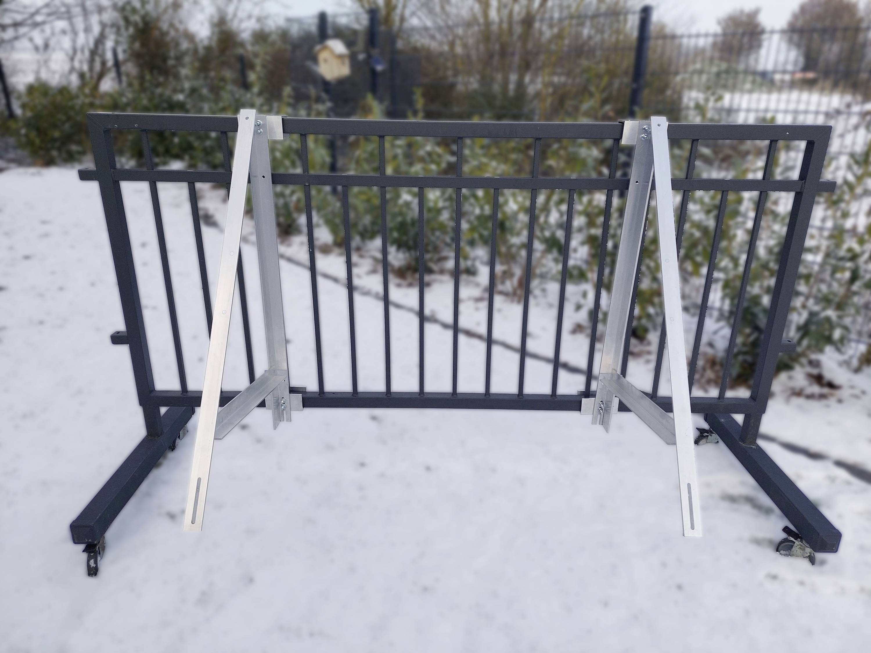 Składana, przenośna metalowa krata stoi w śniegu w ogrodzonym obszarze. W tle widać zimowe drzewa.