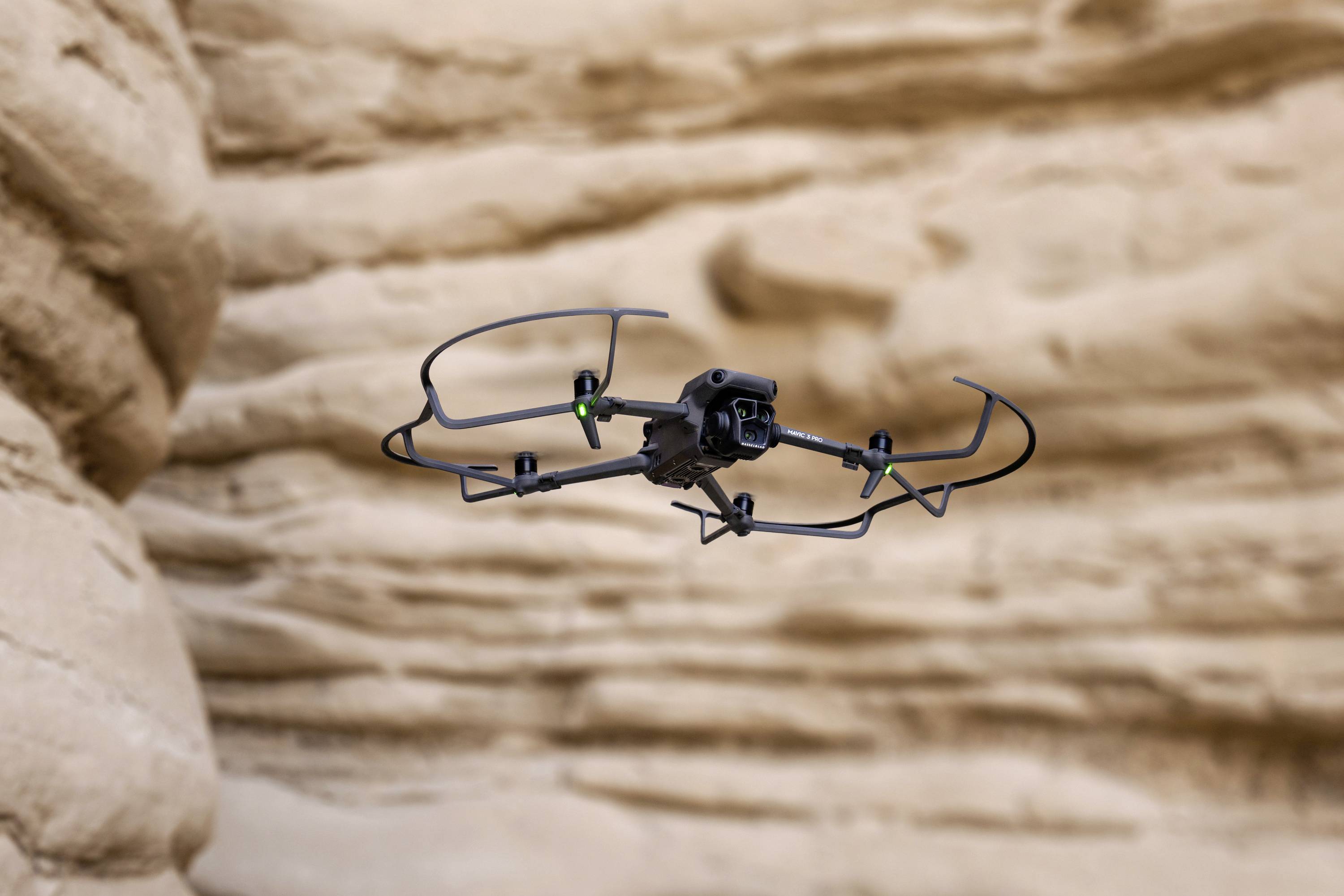 Dron leci przed skalistym, kamienistym krajobrazem. Posiada cztery rotory i zielone diody LED.