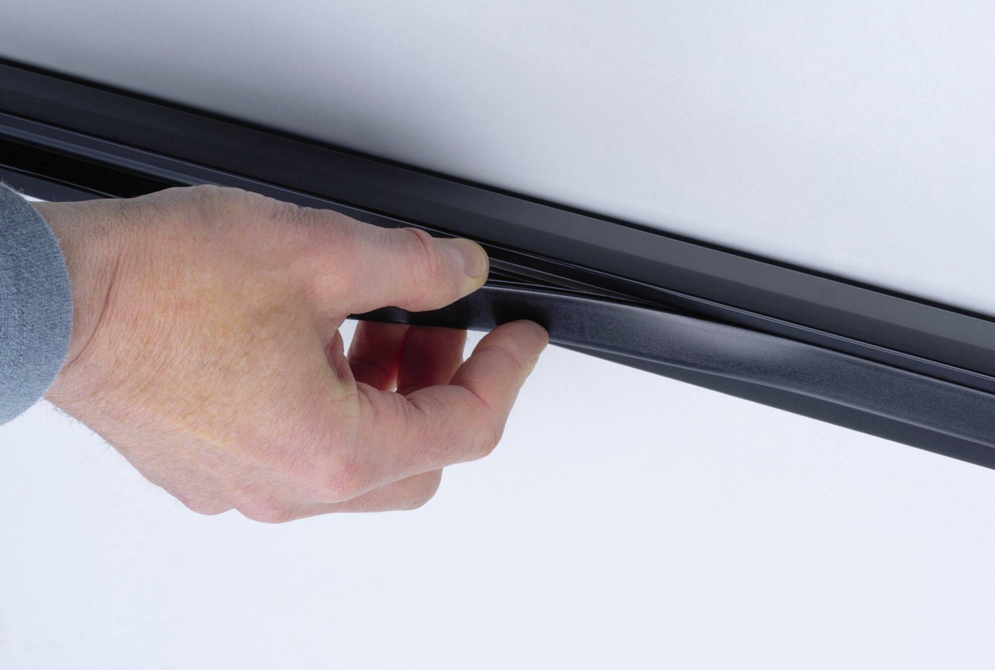 Dłoń odrywa czarny pasek magnetyczny od białej powierzchni.