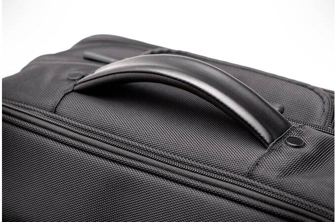 Czarny uchwyt walizki w zbliżeniu na strukturowanym materiale. Uchwyt jest gładki i lekko zakrzywiony.