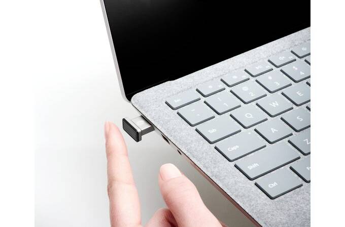 Ręka wskazuje na urządzenie USB podłączone do laptopa. Laptop jest widoczny z boku, prezentując klawiaturę.