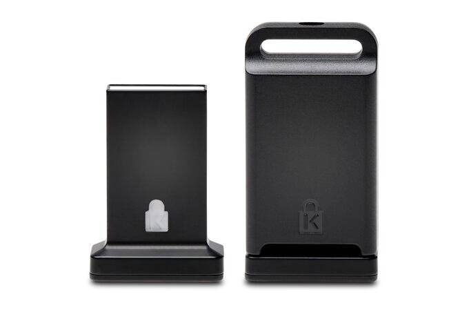 Dwa czarne, stojące urządzenia o kwadratowej podstawie. Po prawej stronie większe z uchwytem, po lewej mniejsze. Logo z motywem zamkowym.