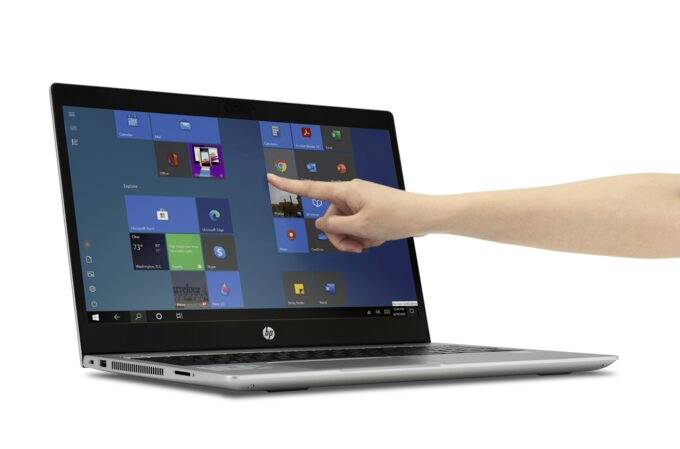 Dłoń wskazuje na ekran laptopa z otwartym menu startowym Windows.