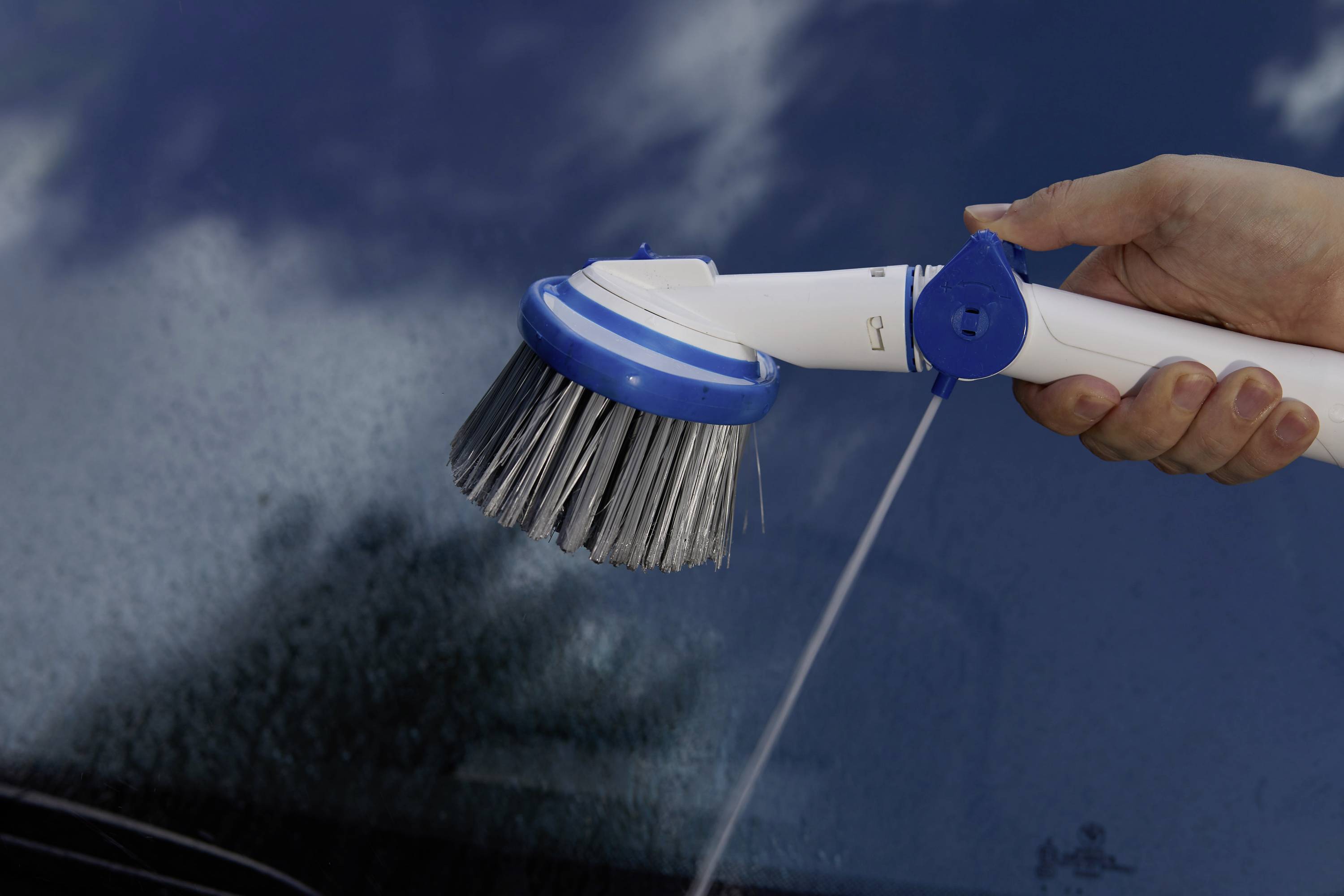 Dłoń trzyma elektryczną szczotkę czyszczącą z dyszą wodną nad mokrą powierzchnią szklaną, aby ją wyczyścić.