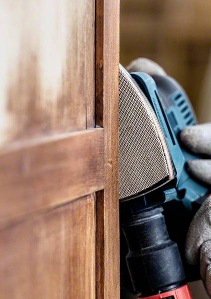 Dłoń trzyma urządzenie ścierne, które wygładza drewnianą powierzchnię. Zbliżenie ukazuje precyzyjną pracę nad elementem meblarskim, z widocznymi plastikowymi detalami narzędzia.