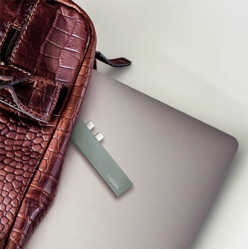 Czerwone skórzane etui leży na srebrnym laptopie, do którego podłączony jest pendrive.