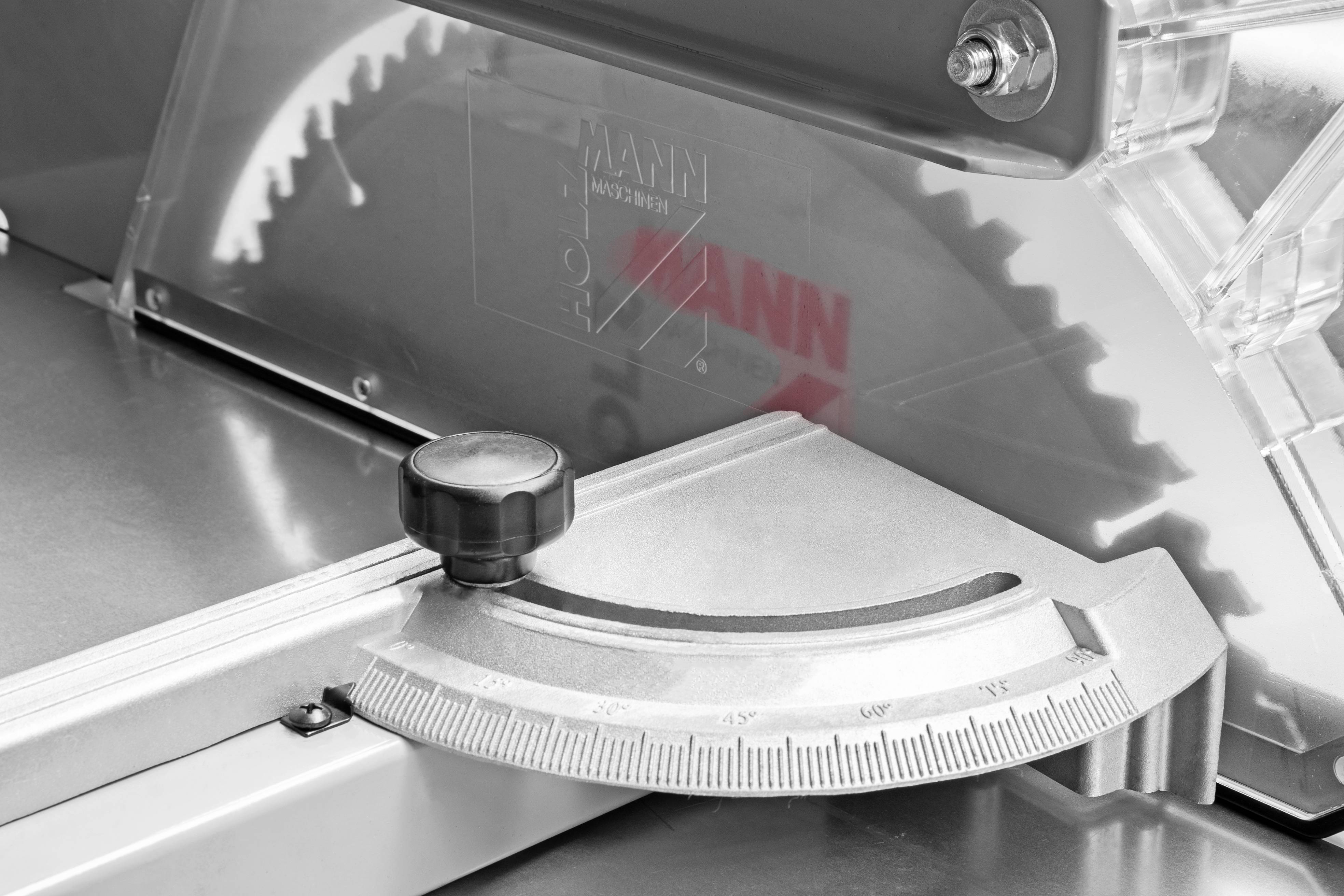 'Zbliżenie stołu pilarki tarczowej z podziałką i uchwytem do regulacji kąta. Części piły tarczowej są częściowo widoczne.'