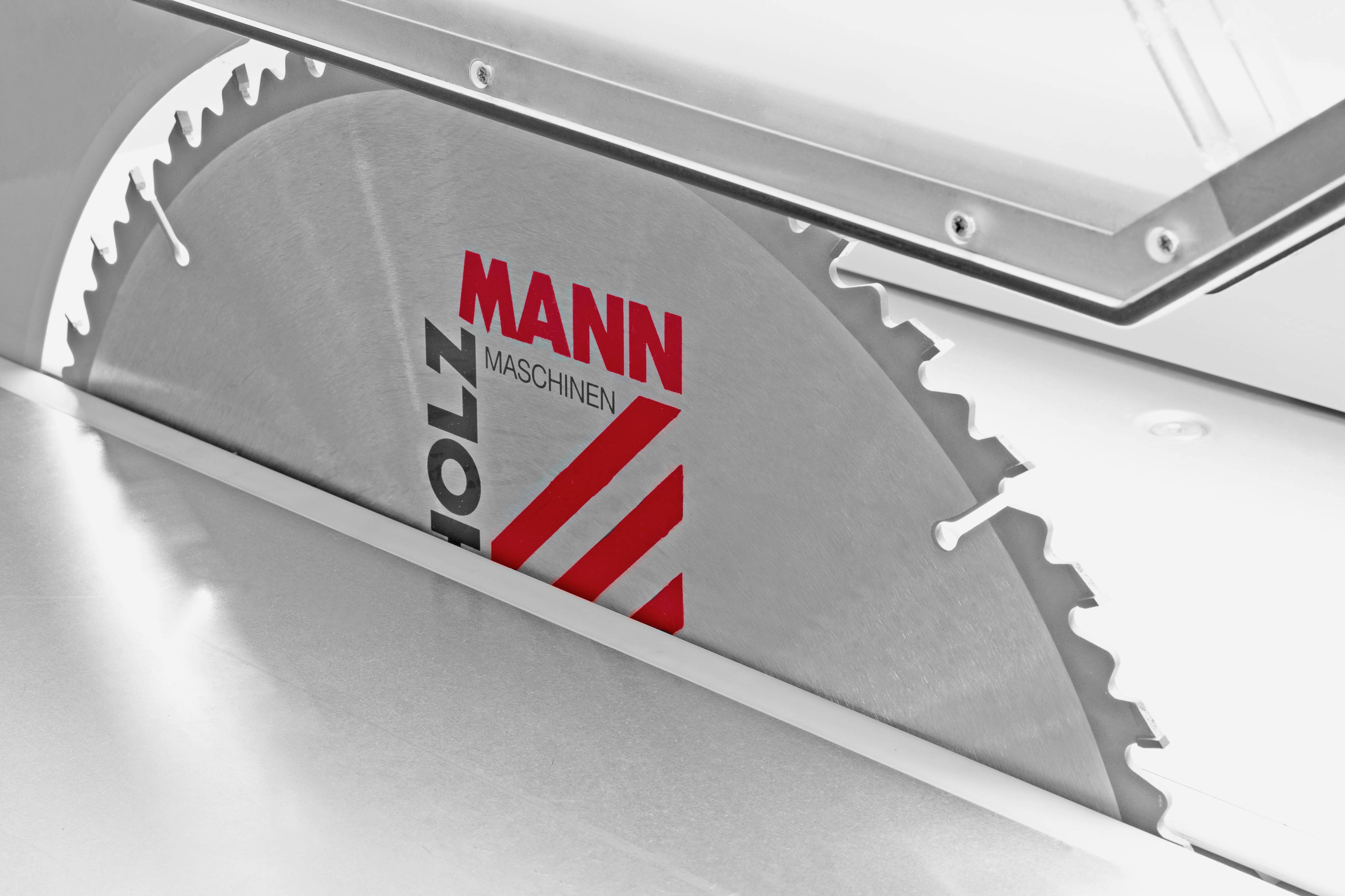 Zbliżenie tarczy piły okrągłej z napisem 'HOLZMANN MASCHINEN' i czerwonymi paskami, częściowo otoczonej stołem.