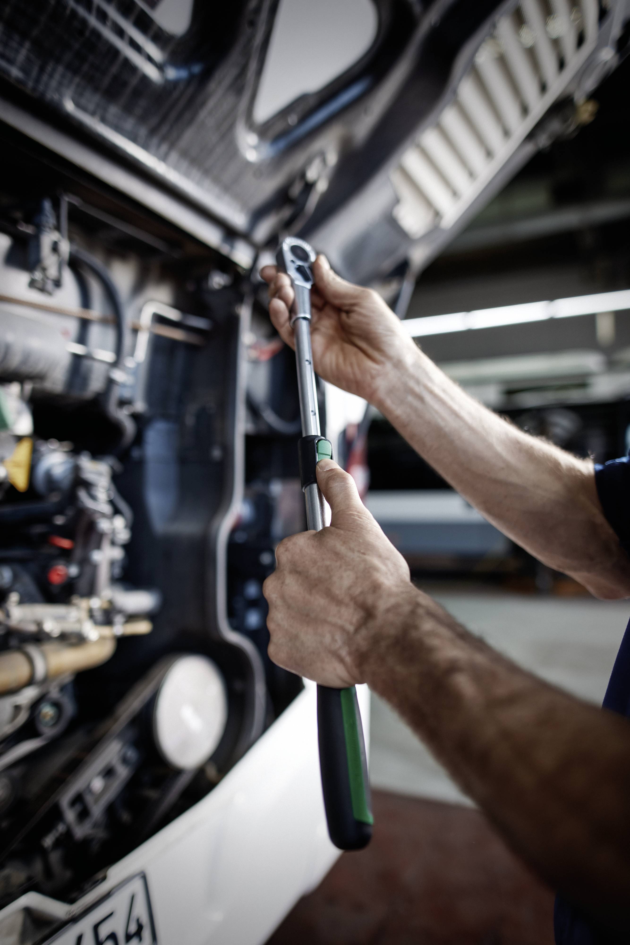 Osoba reguluje duży klucz na silniku ciężarówki, koncentrując się na konkretnym elemencie. Zdjęcie podkreśla prace naprawcze mechaniczne.