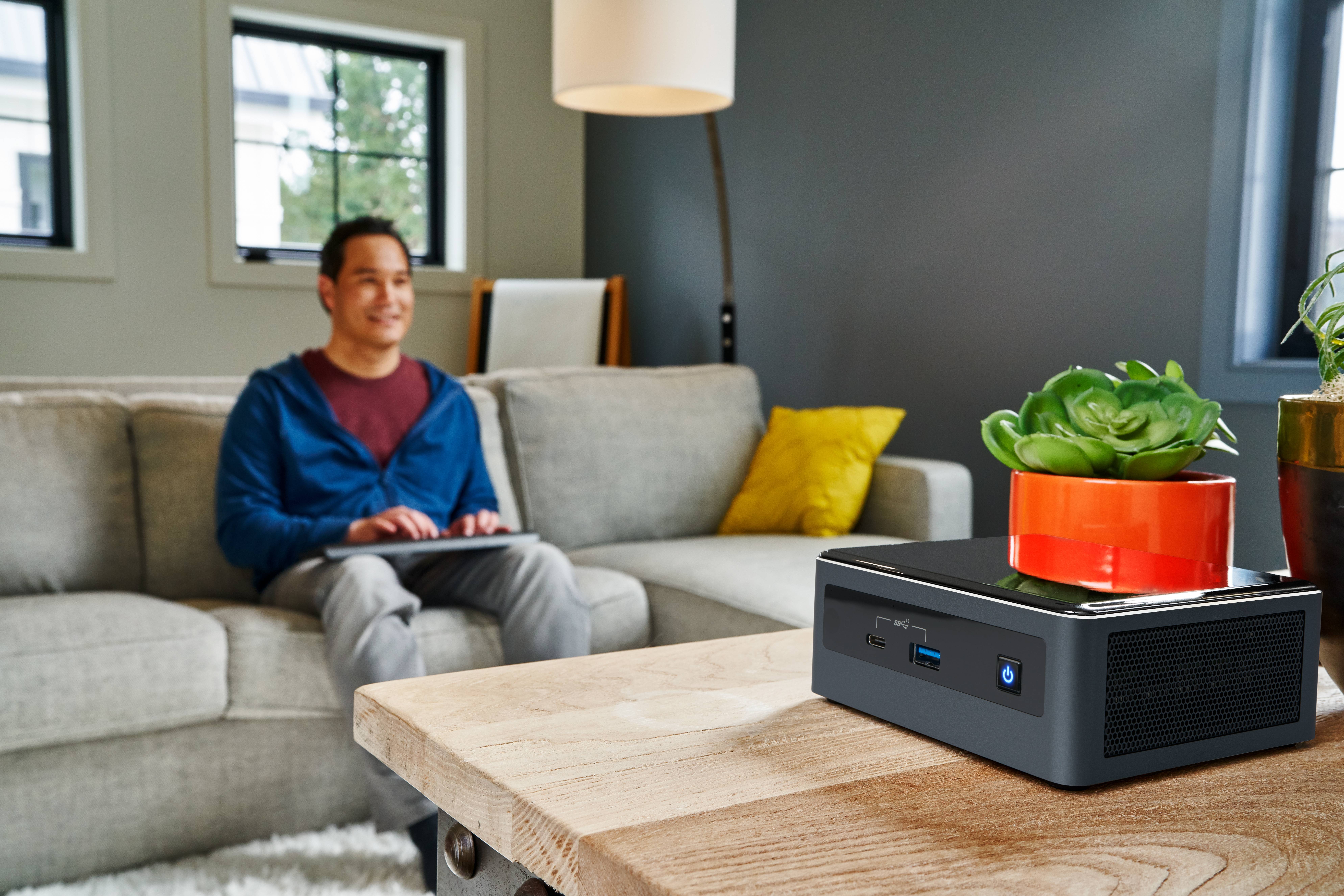 Mężczyzna siedzi na kanapie w nowoczesnym salonie i korzysta z tabletu. Na pierwszym planie, na stole, stoi minikomputera.