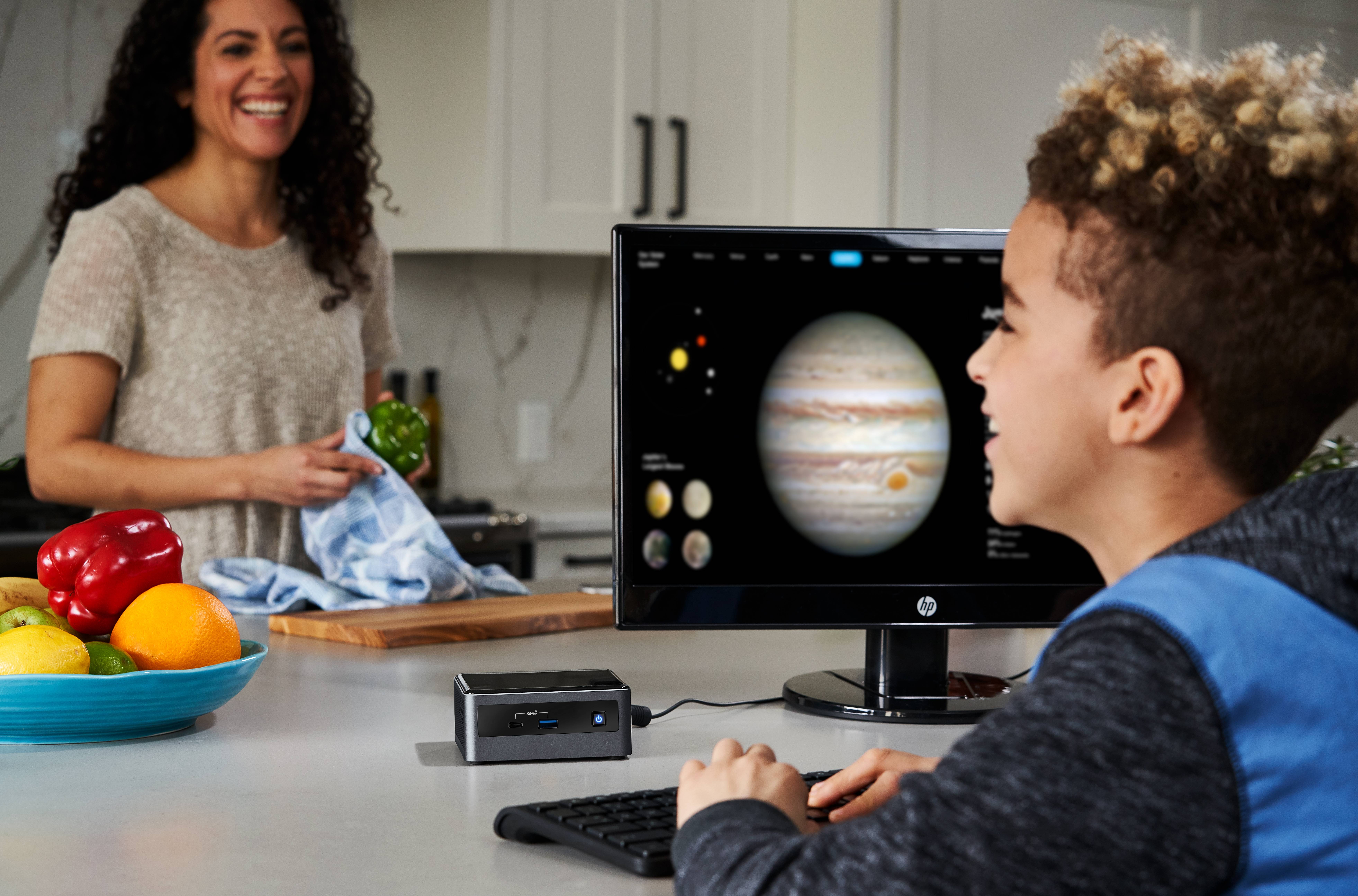 Chłopiec uśmiecha się, oglądając zdjęcia Jowisza na ekranie komputera. W tle kobieta przygotowuje posiłek w kuchni.