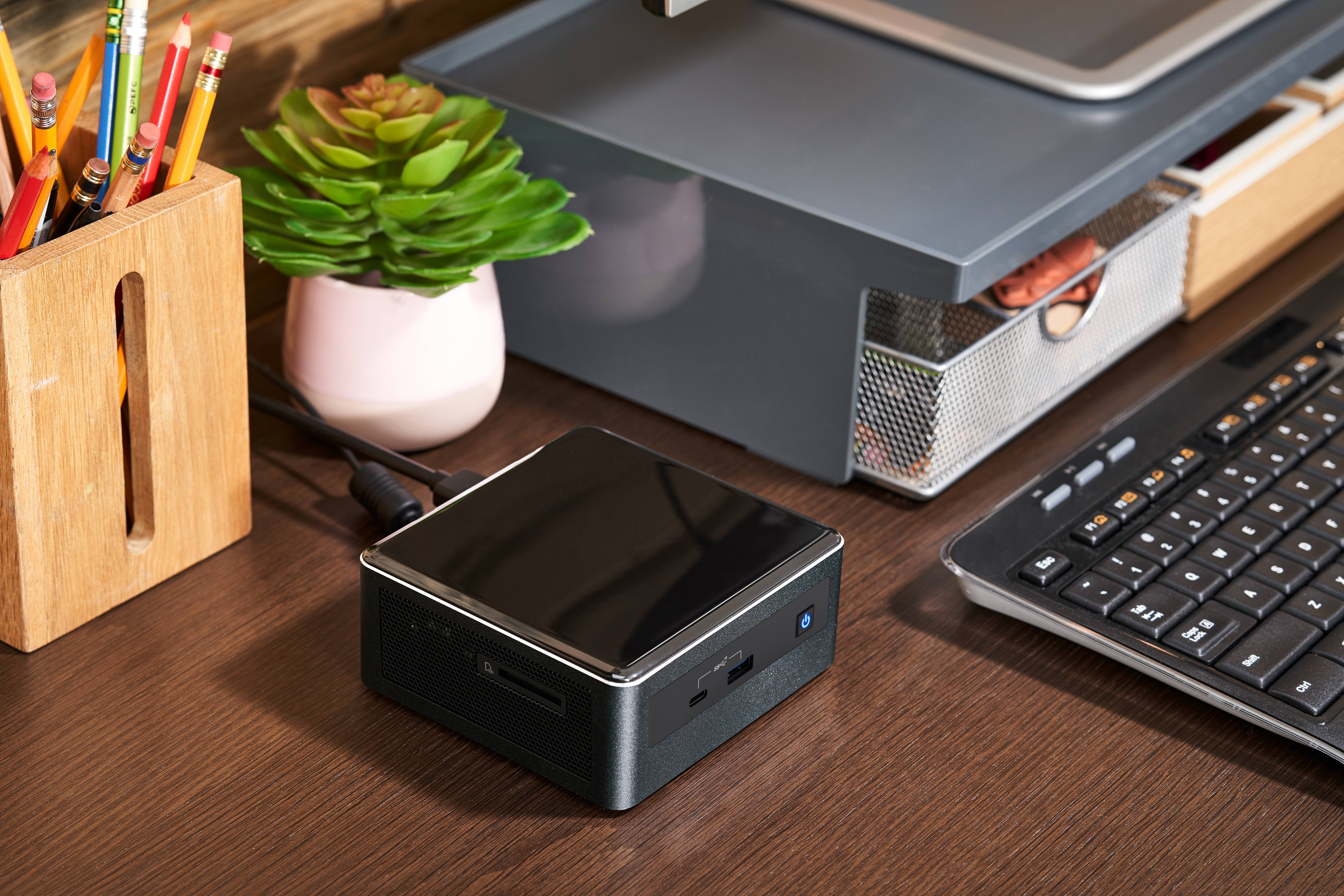 Czarny mini komputer stoi obok klawiatury na biurku, w pobliżu znajduje się bukiet kwiatów i pojemnik na długopisy.